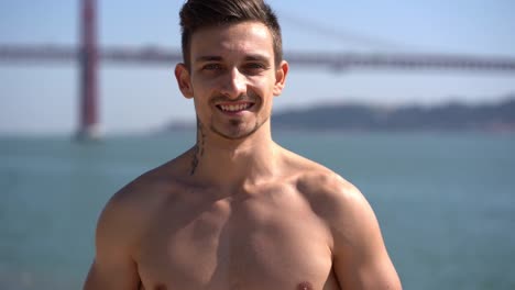 guapo deportista de pecho desnudo sonriendo a la cámara al aire libre