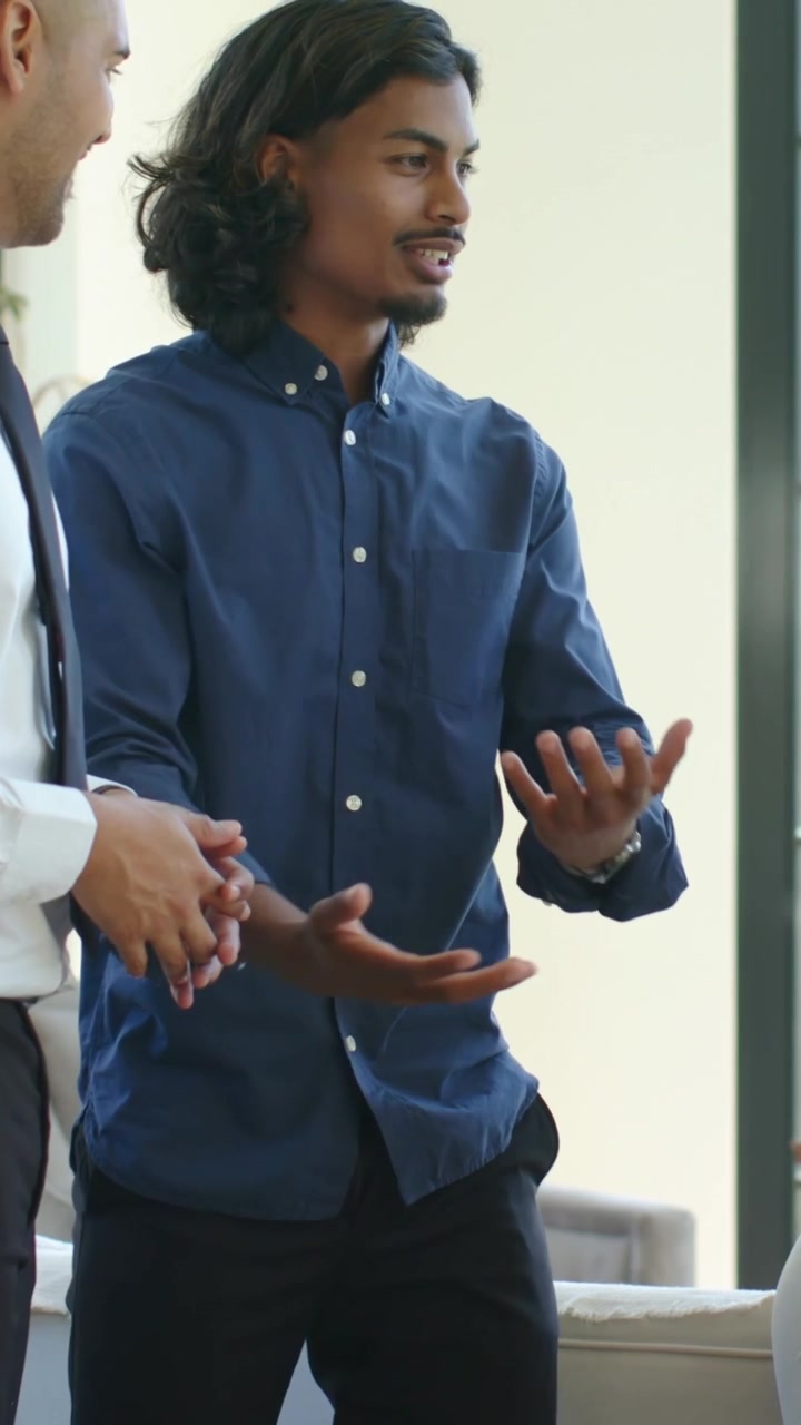 Vertical video: After cue, navy-shirt man explaining to group in lounge, listener in tie