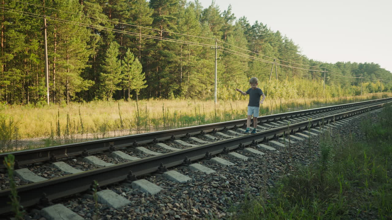 calm kid walking carefully on railway beam, arms extended to maintain balance, with background of forest, grassy terrain, and visible power lines under clear sky in peaceful outdoor environment