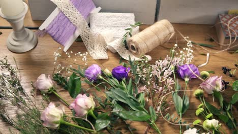 vista desde arriba: mesa de madera con flores, tijeras, cintas, papel de decoración y otras herramientas para el arreglo de ramos en