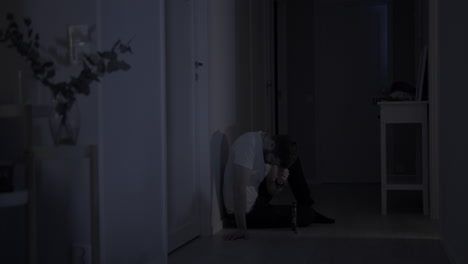 depressed man in grief sits alone on home floor leaning against dark wall