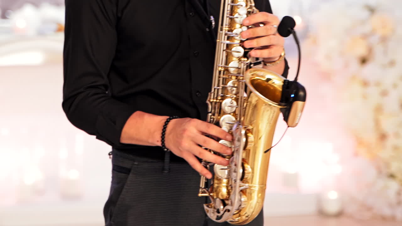 Saxophonist plays on golden saxophone indoors. A young man in black clothes is playing on a modern sax with microphone at the party. Jazz music. Close-up