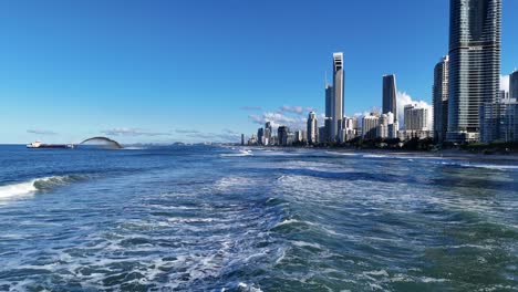a dredger pumps sand near gold coast's skyline under clear skies, creating dynamic water patterns