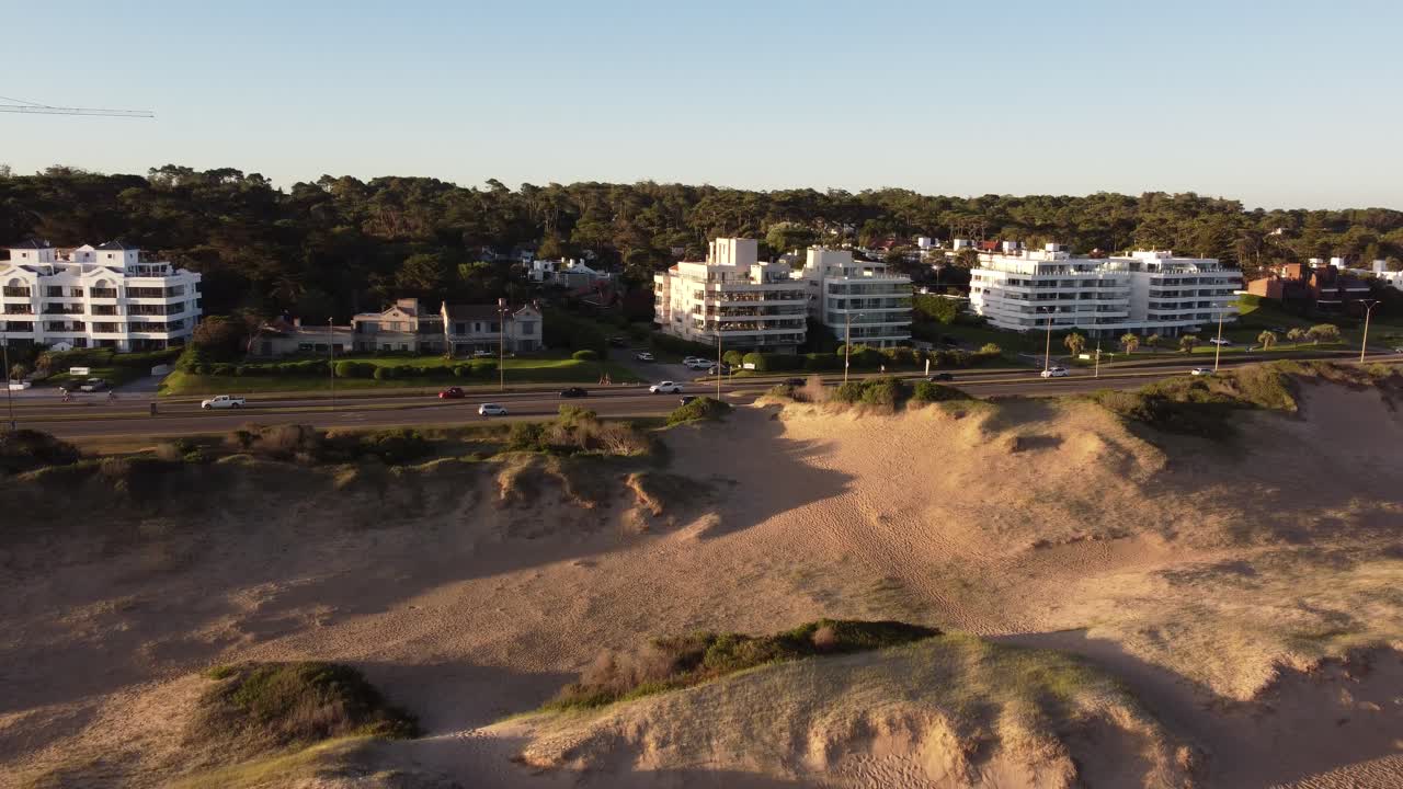 toma lateral aérea de casas de lujo y carreteras en la ciudad de punta del este durante la puesta de sol dorada - dunas de arena en primer plano