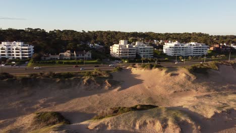 aerial lateral shot of luxury houses and road in punta del este city during golden sunset - sandy dunes in foreground