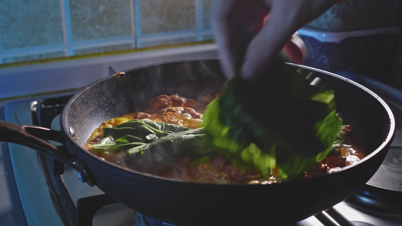agregando hojas de espinacas frescas a la pechuga de pollo en salsa de queso y mayonesa cocinando en una sartén