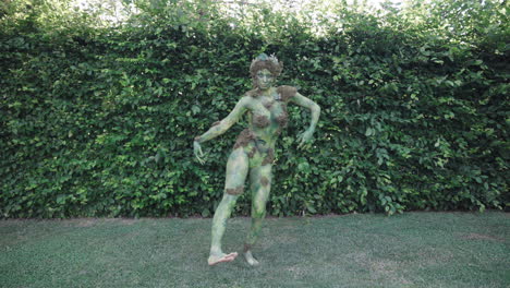 female bodypaint model dancing and moving slowly and sensual in a garden - wide shot