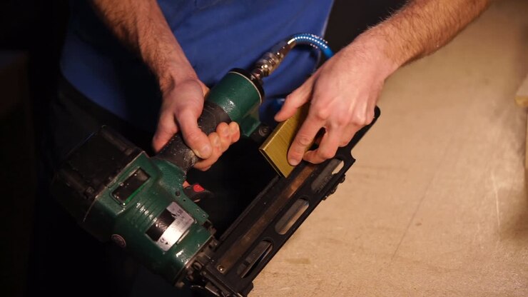 Man using a nail gun to assemble wooden boards.