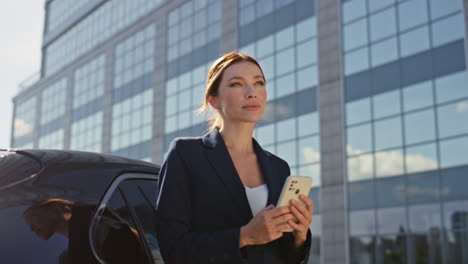 attractive entrepreneur reading message on mobile phone leaning at car close up.