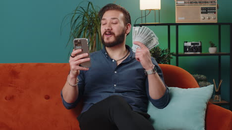 smiling happy lebanese man counting money cash use smartphone, income saves lottery win budget