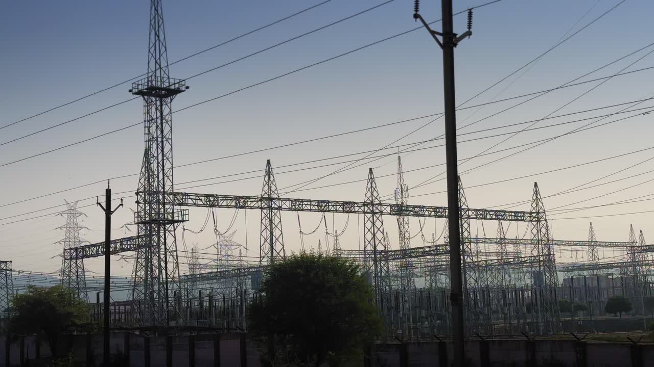 Static view of a vast high-voltage substation filled with steel towers, power lines, and dense wiring structures silhouetted against the soft early sky