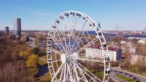 a smooth aerial circle around the white ferris wheel in riga, with the scenic river city in the background.