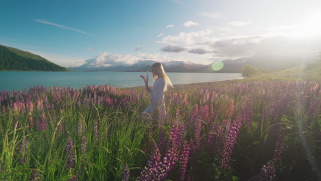 Woman-walking-through-fantasy-scenery-in-magical-flower-field-at-alpine-lake