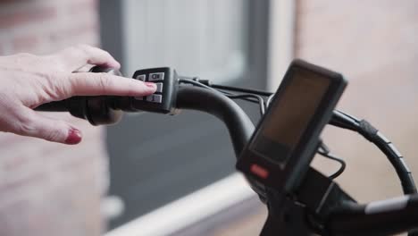 close up of a woman's hand turning on the power to a electric bicycle with the buttons on the handle bars