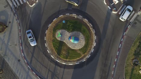 vista aérea de arriba hacia abajo del avión no tripulado de la rotonda de tráfico o el círculo de tráfico de la carretera con árboles verdes junto a las aceras y la hierba verde
