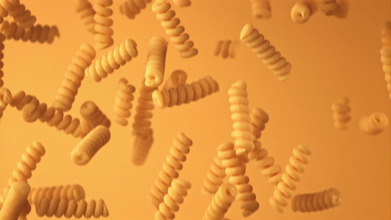 Raw Fusilli Pasta Pieces Falling in Slow Motion on Orange Background