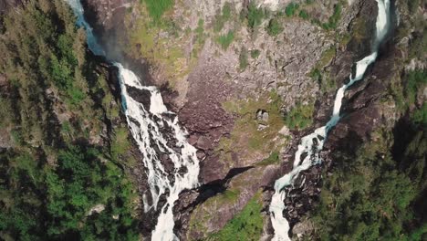 Bird's-eye-view-drone-shot-of-a-large-waterfall-in-Norway-and-a-green-forest-in-the-background