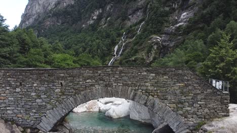 mountain river streaming underneath old cobblestone bridge in switzerland, ascend view