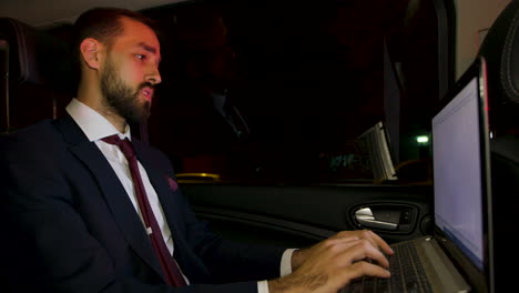 businessman in suit working late on his laptop on the back seat of his car