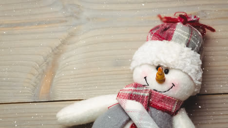 snow falling over close up of snowman toy on wooden surface