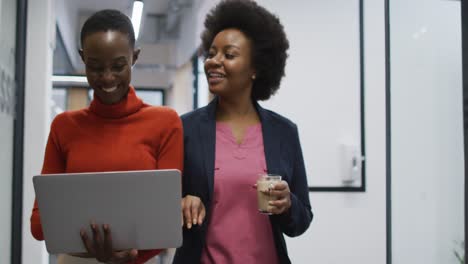 two african american female office colleagues with laptop discussing together at office