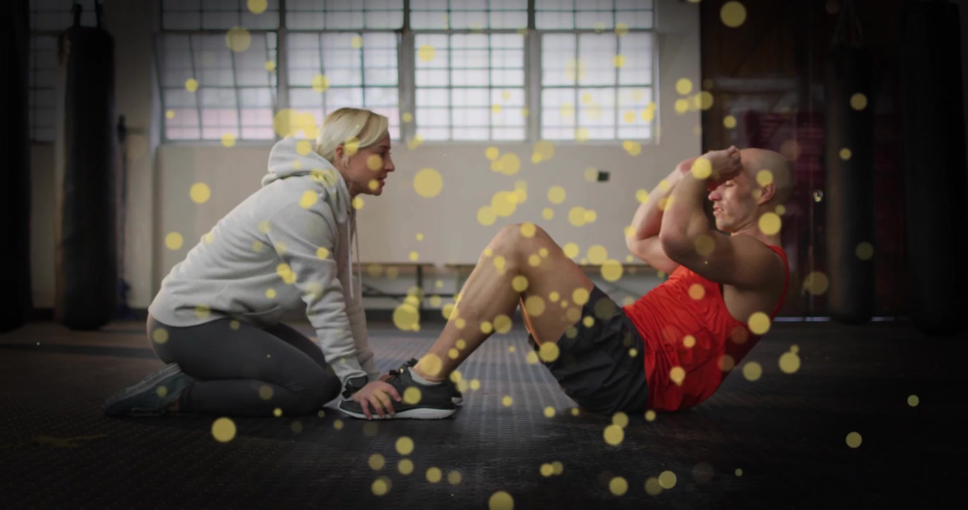 Trainer leitet Trainierenden bei Crunches im Fitnessstudio für Rumpfstärke an, mit schwebenden goldenen Partikeln.
