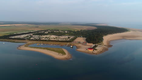 Einrichtung-Eines-Drohnenschusses,-Der-Bei-Flut-über-Das-Meer-Fliegt,-Mit-Bach--Und-Rettungsboothaus-Und-Statischem-Wohnwagenpark-In-Wells-next-the-Sea-North-Norfolk-UK-Ostküste