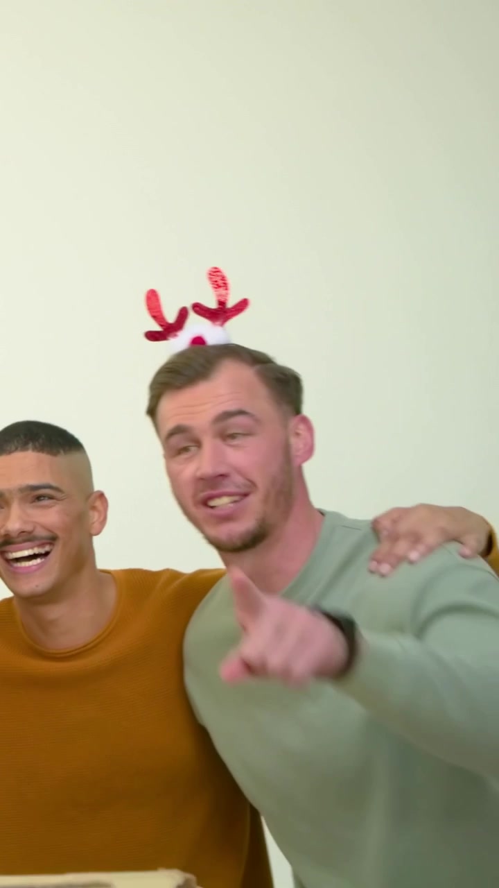 Video verticale: Uomini sorridenti in una stanza, con una fascia che appare, che si tengono per le braccia, l'uomo a destra che festeggia sopra una scatola.
