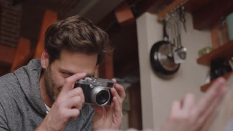 Feliz-Pareja-Joven-Tomando-Fotos-Juntos-Usando-Una-Cámara-Divirtiéndose-En-Casa-En-El-Sofá-Disfrutando-Juguetonamente-De-Una-Relación-Romántica-Fotografiándose-Unos-A-Otros-Haciendo-Muecas