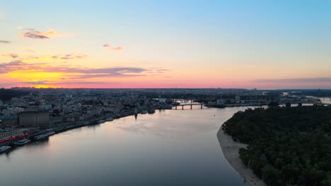 Drohnenansicht-Des-Flusses-Dnipro-Mit-Der-Stadt-Kiew-Während-Des-Sonnenuntergangs