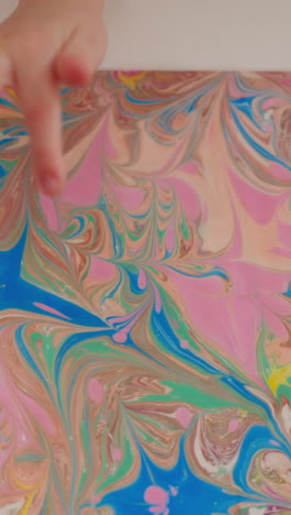 little girl finger points to stylish painting with bright marbling patterns on table in classroom upper closeup slow motion. turkish ebru technique studying