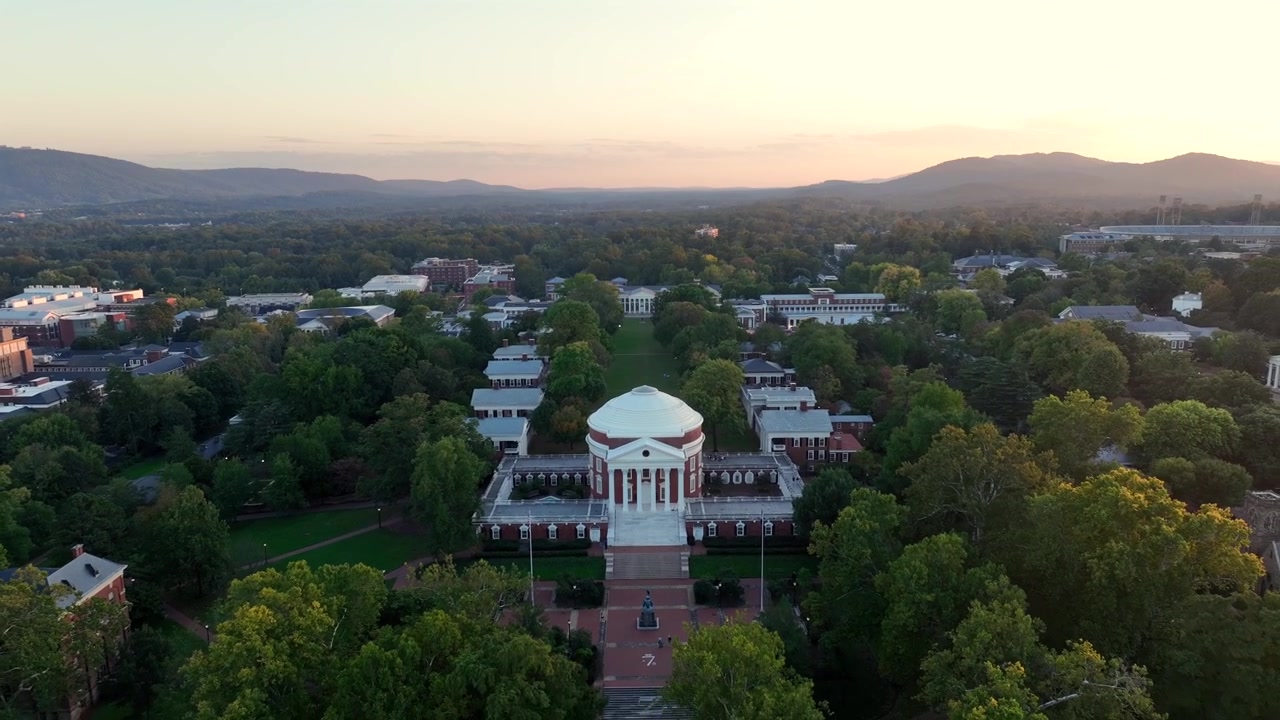 Aerial backwards Shot of University of Virginia with campus and historic cupola Building. Sunset time in american town with mountains in autumn season. Wide shot.