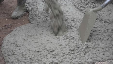 closeup of wet concrete being poured on the ground as workers pave a street