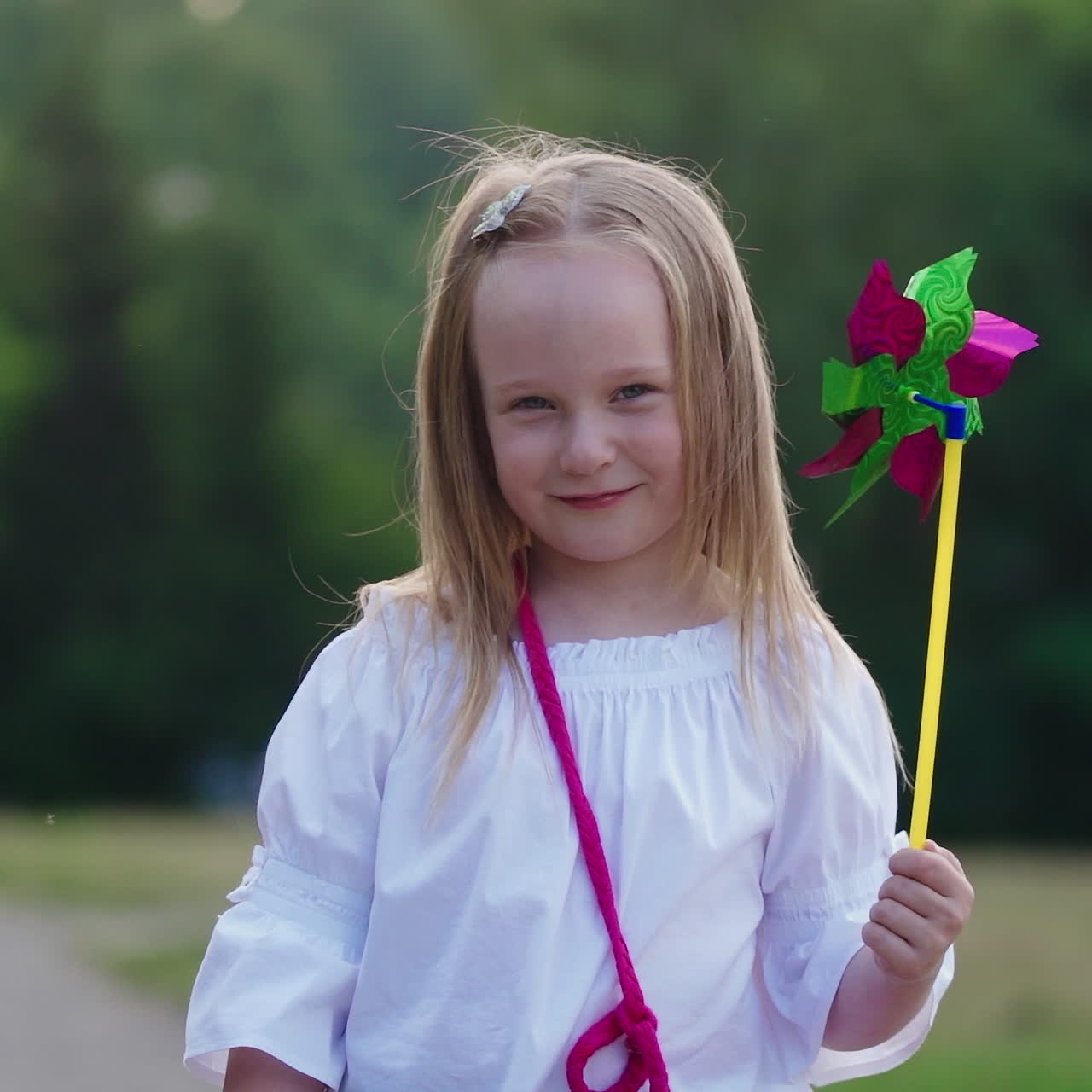 Lovely girl posing to camera. Positive little girl closing her face with toy windmill in the park. Nice child with colorful toy outdoors in summer.