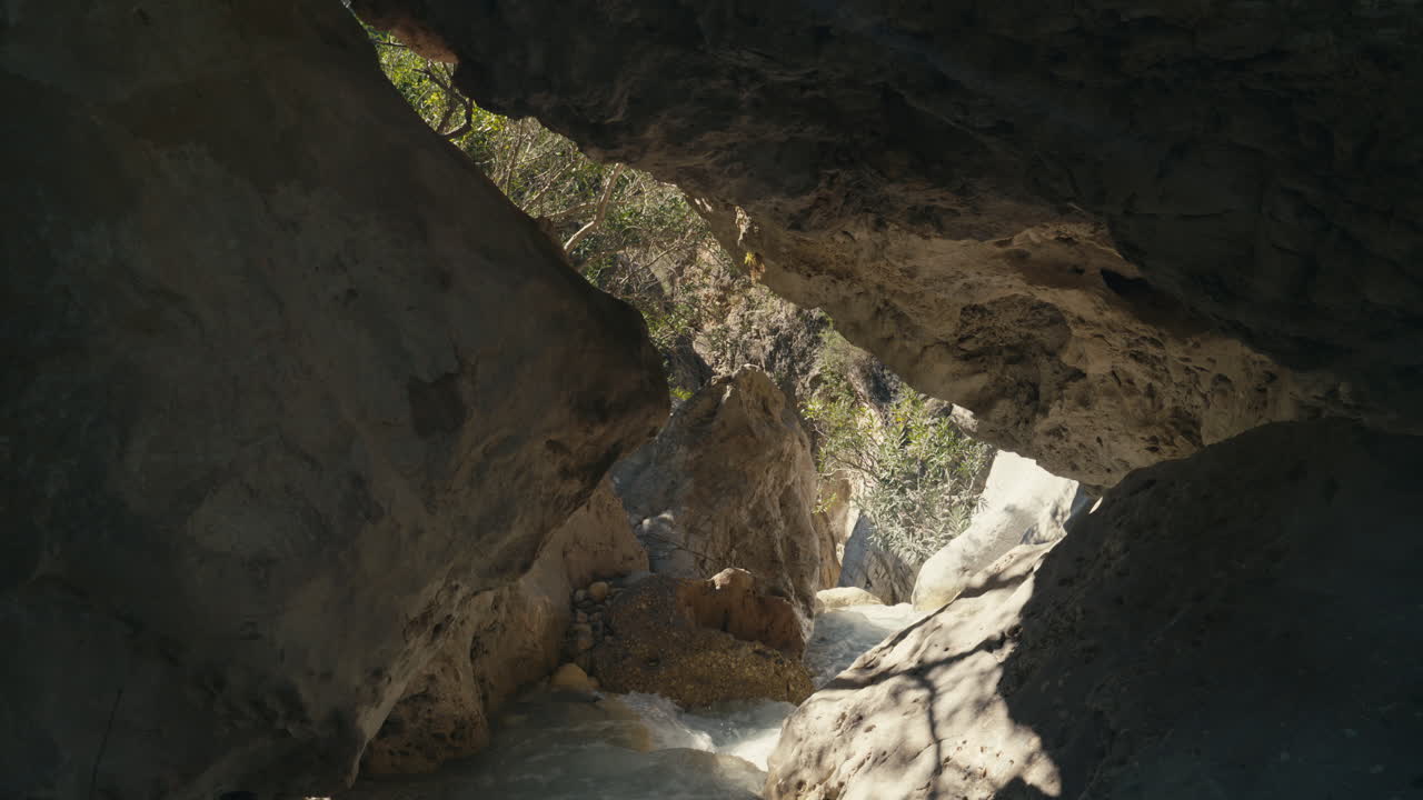 Fiume limpido che scorre attraverso uno stretto passaggio di canyon incorniciato da grandi rocce. Formazione naturale a tunnel con la luce del sole che filtra, creando un'atmosfera coinvolgente e avventurosa