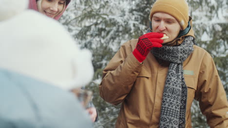 cheerful friends eating and speaking while camping in winter