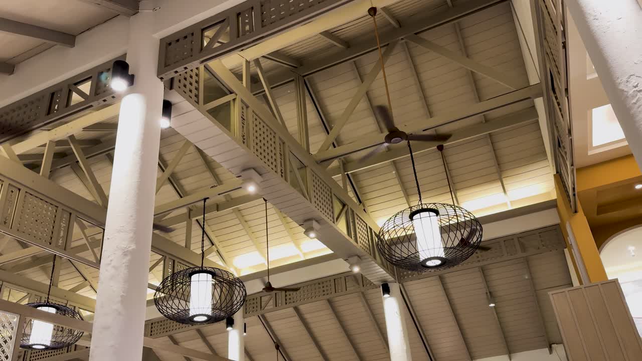 los ventiladores de techo giran en una sala de vacaciones al aire libre bien iluminada con vigas estructurales visibles e iluminación ambiental