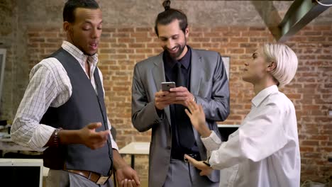 three multy-ethnic workers dancing in office, watching smartphone, company party concept