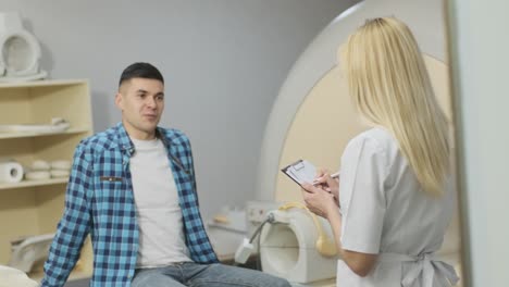 la radióloga tiene un diálogo con el paciente joven, pregunta y toma nota del historial médico del paciente, las quejas en la clínica moderna junto con la mri de tipo cerrado moderna