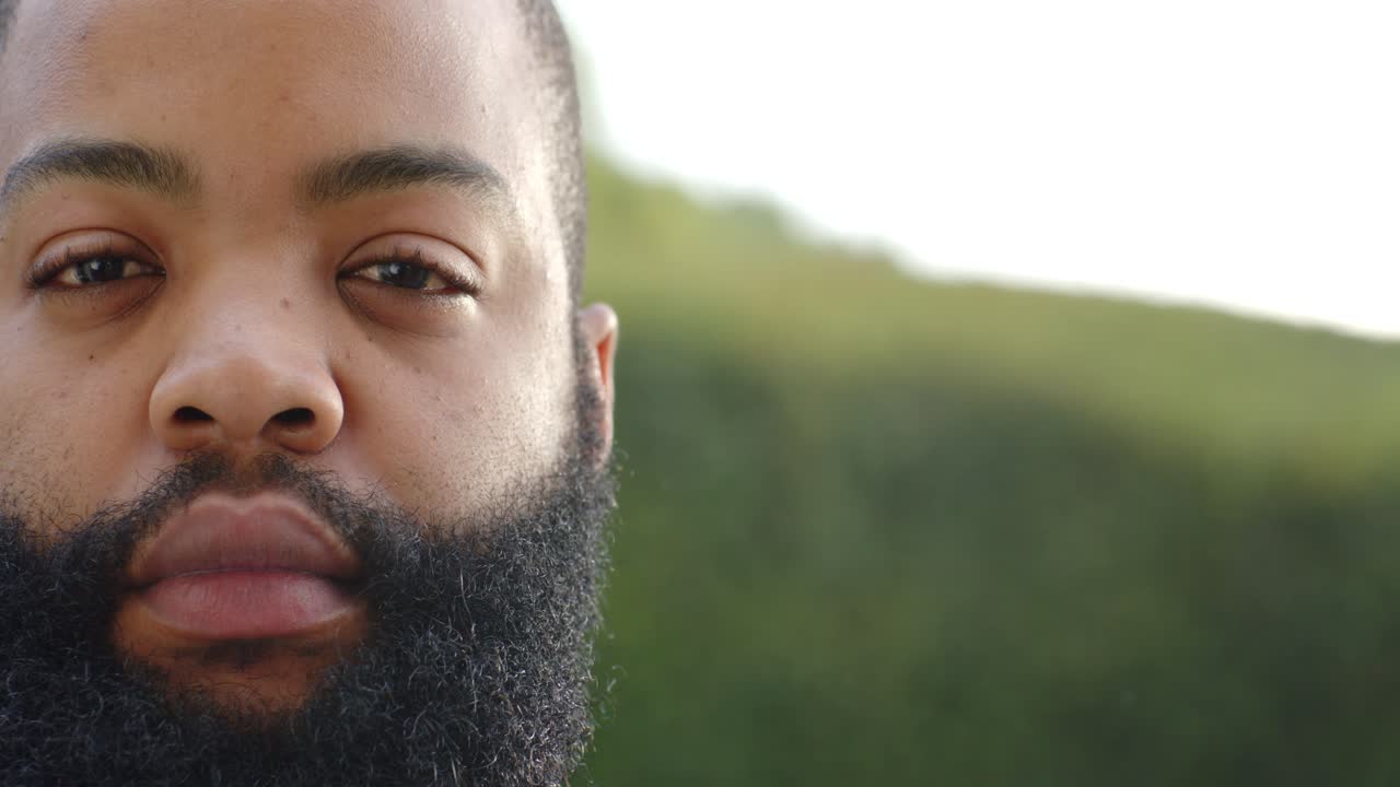 Voksen afrikansk mann ved hekken åpner øynene sakte mens kameraet beveger seg, viser skjegg og blå krage.