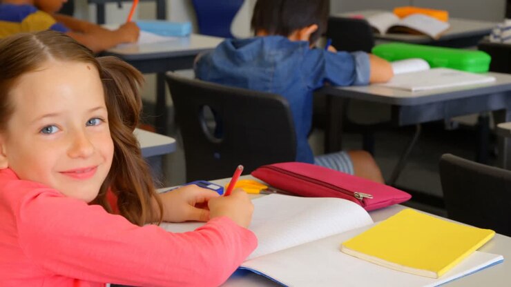 Escolar caucásica feliz estudiando en un pupitre en un aula de la escuela 4k