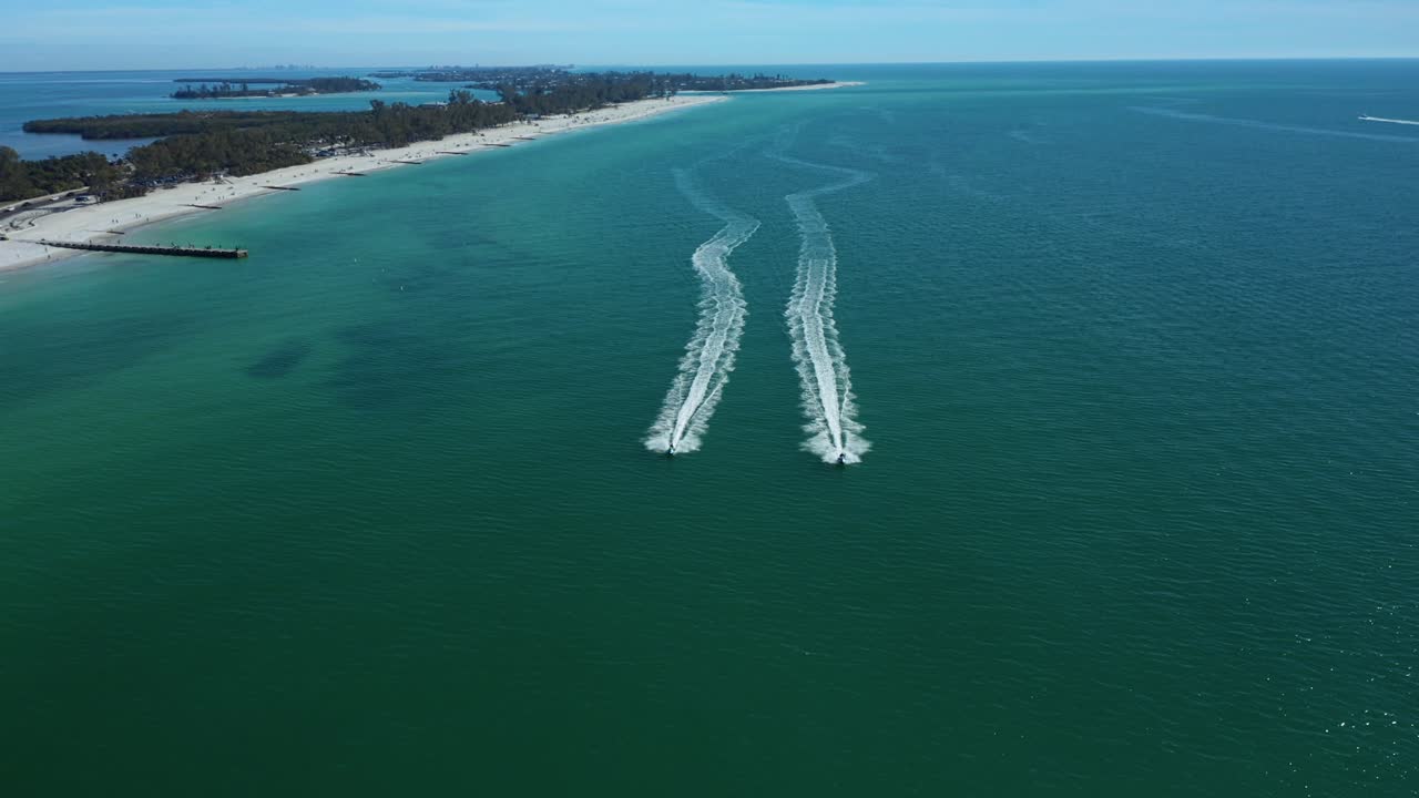 Due motoscafi lasciano scie distinte mentre corrono parallelamente lungo l'ampia costa di Bradenton Beach. Ideale per contenuti di viaggio e avventura