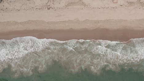 bird's eye dolly shot of gentle waves on a white sand beach in malibu, california. 4k at 30 fps