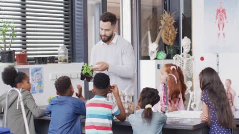 Diverse-male-teacher-and-happy-schoolchildren-having-ecology-class-in-school-classroom