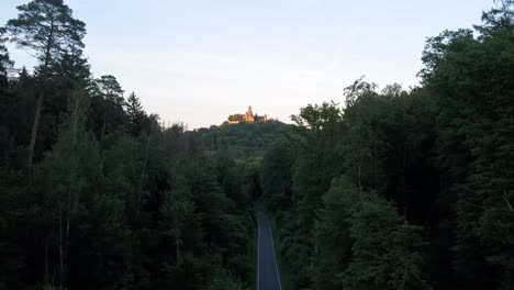 drone flight between the woods flying towards view of braunfels castle and a car passing on the road in germany
