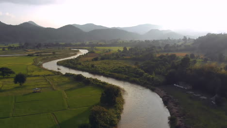 Aerial-flight-above-river-and-Rice-fields-against-mountains-on-horizon-during-sunset-time-Film-Graded