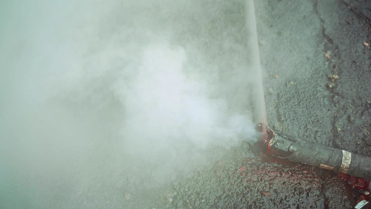 A hot water flow on the asphalt from a burst pipe creating steam in a cold weather. Breakthrough tubes. Emergency situation. Close-up.