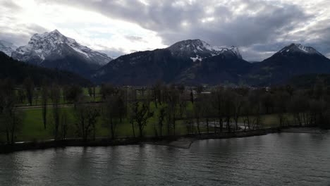 Pullback-from-lake-shoreline-with-leafless-trees-as-water-reflects-cloudy-sky-texture