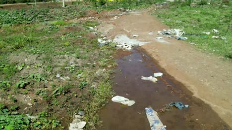 steady forward low angle of dirty water pools with garbage and waste on african dumping site during summer