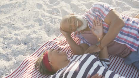 happy senior african american couple lying on blanket at beach, slow motion